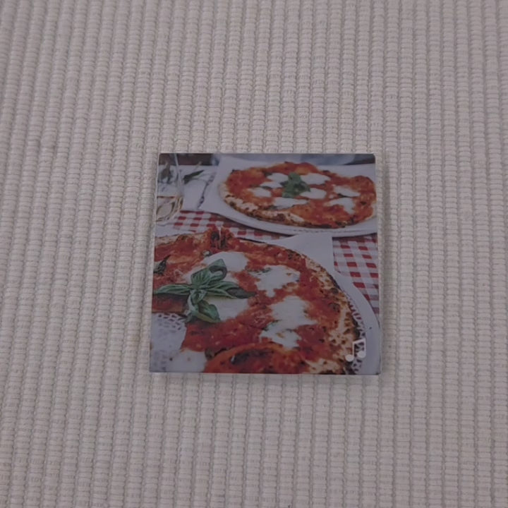 video pointing their finger to a photo magnet with a picture of beautiful italian pizza on it. They are bringing the viewers attention to a  music logo in the bottom right corner. they then scan the magnet with the back of their phone and it brings up a website for a classic pizza dough recipe