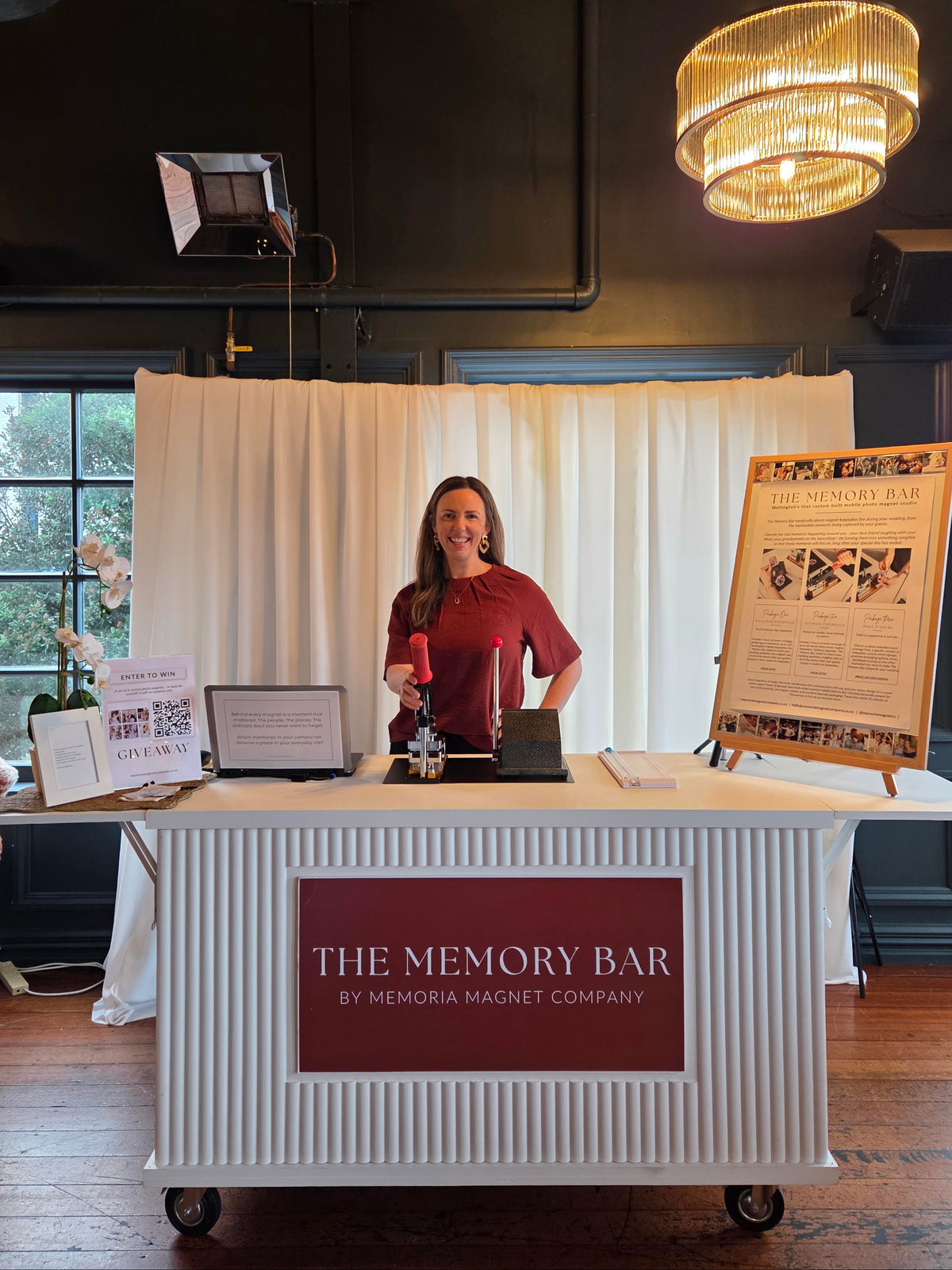 photo of the Memory Bar all set up at an event. Christina, the company founder, is standing behind it in front of a beautiful draped backdrop  