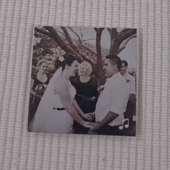 Video of a custom photo magnet which is of a couple on their wedding day. a finger points to a music logo in the bottom right corner. a phone then scans the magnet with the back of the phone and a link to a youtube video with the couple's wedding song begins to play