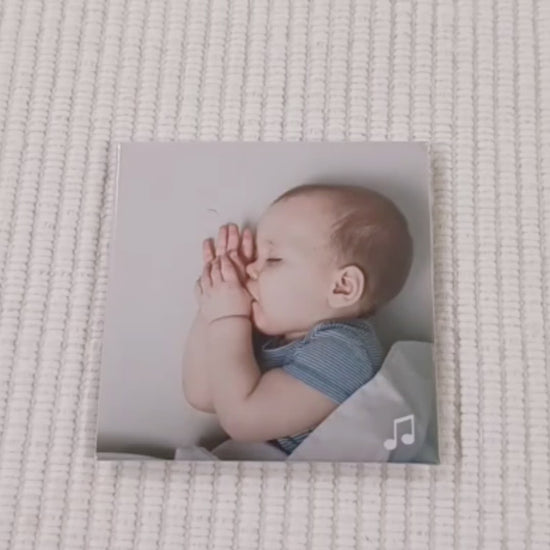 this is a video of a custom photo magnet which is a picture of a baby sleeping sweetly sucking their thumb. a finger points to a music icon in the bottom right corner and a phone then scans the magnet. a spotify link loads on the screen and You are my Sunshine song begins to play