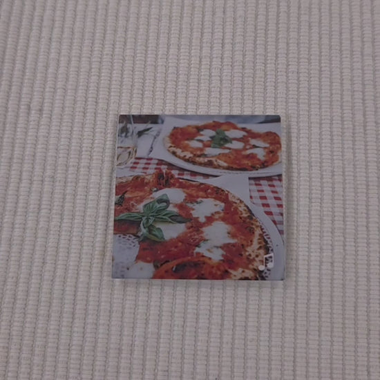 video pointing their finger to a photo magnet with a picture of beautiful italian pizza on it. They are bringing the viewers attention to a  music logo in the bottom right corner. they then scan the magnet with the back of their phone and it brings up a website for a classic pizza dough recipe